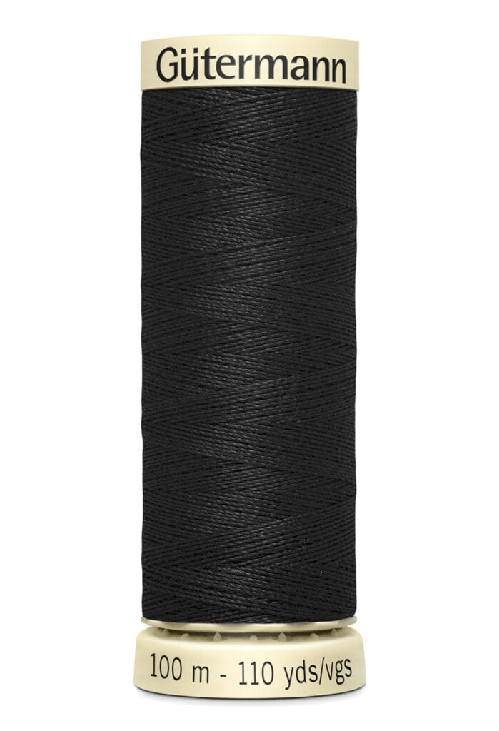 A spool of Gütermann black sewing thread labeled "100 m - 110 yds/vgs." The label and spool ends are cream-colored, providing contrast with the dark thread.
