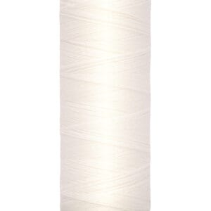 A spool of Gutermann sewing thread in a light cream color, labeled 100 meters and 110 yards, is standing upright. The thread is neatly wound, and the spool has a light yellow base and top with black text.