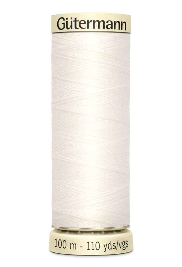 A spool of Gutermann sewing thread in a light cream color, labeled 100 meters and 110 yards, is standing upright. The thread is neatly wound, and the spool has a light yellow base and top with black text.