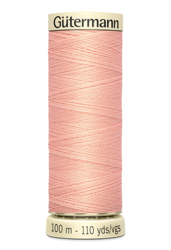 A spool of Gütermann thread in light pink, featuring a crisscross pattern. The base indicates the length as 100 meters or 110 yards.