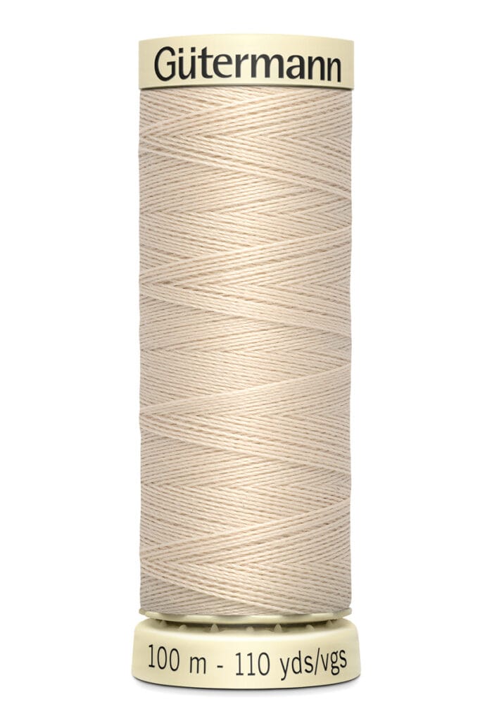 Spool of Gütermann sewing thread in beige, wrapped tightly around a cylindrical cream-colored spool. Labeled with "Gütermann" and "100 m - 110 yds/vgs.