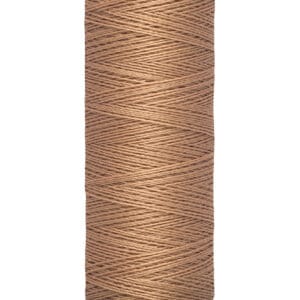 A spool of Gütermann brown thread, labeled with "100 m - 110 yds/vgs" on the base. The thread is neatly wound around the cylindrical spool, in a light beige tone.