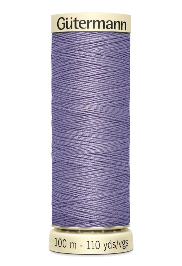 A spool of Gütermann sewing thread in light purple, labeled with "100 m - 110 yds/vgs." The spool is beige with the brand name written on top. The thread is wound neatly around the spool.
