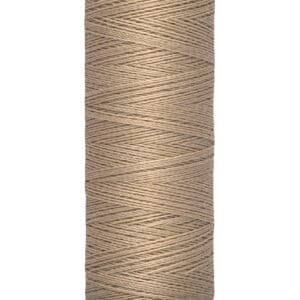 A spool of Gütermann thread in a beige color. The thread is neatly wound, and the spool label shows "100 m - 110 yds/vgs.
