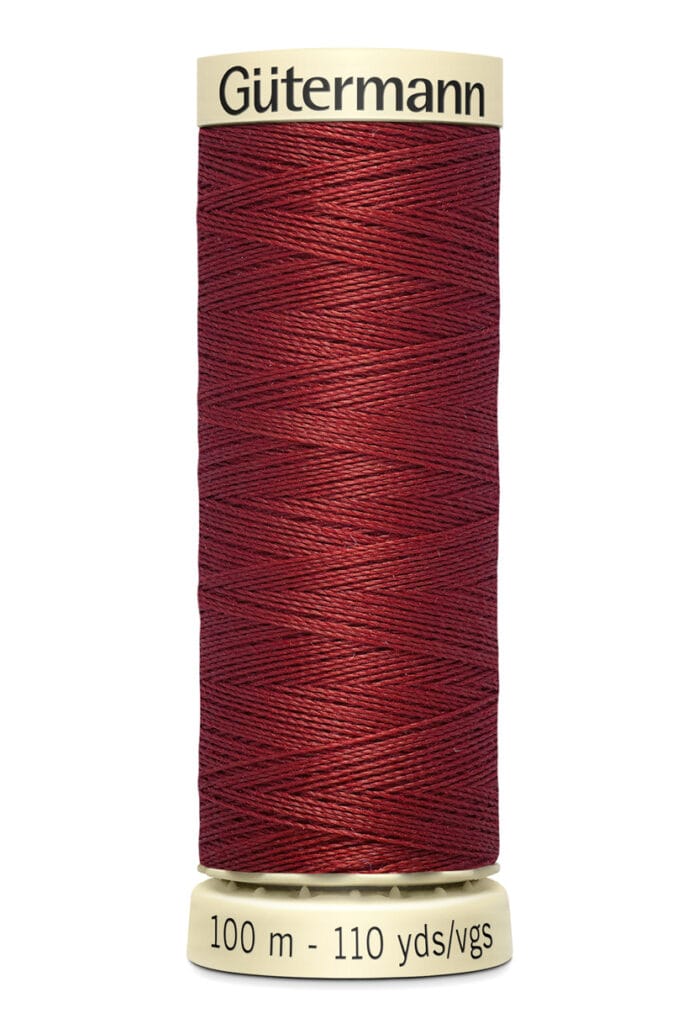 A spool of Gütermann thread in dark red, containing 100 meters or 110 yards of thread. The spool is cylindrical with light beige ends, and the thread is neatly wound around it.