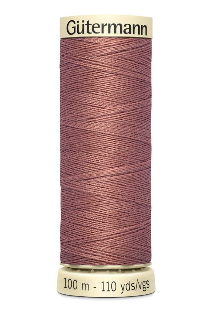 A spool of Gütermann thread in a dusty rose color is shown. The label indicates the length as 100 meters, or 110 yards. The spool is cylindrical with a beige top and bottom.
