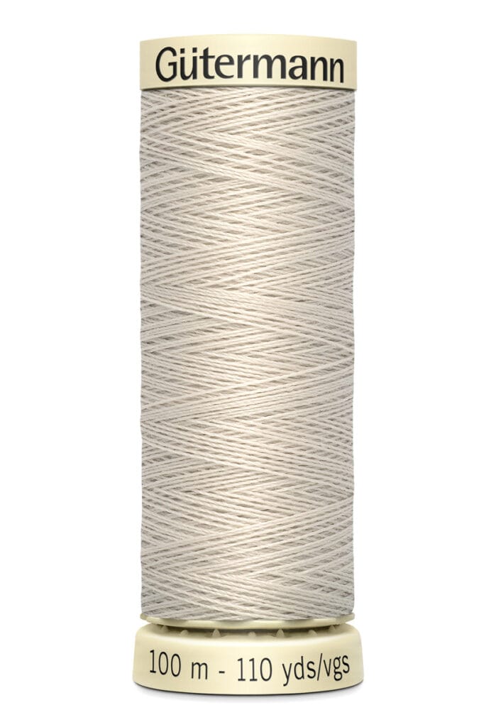 A spool of Gütermann thread in light beige, labeled with 100 meters and 110 yards. The spool is designed with narrow grooves to hold the thread securely.