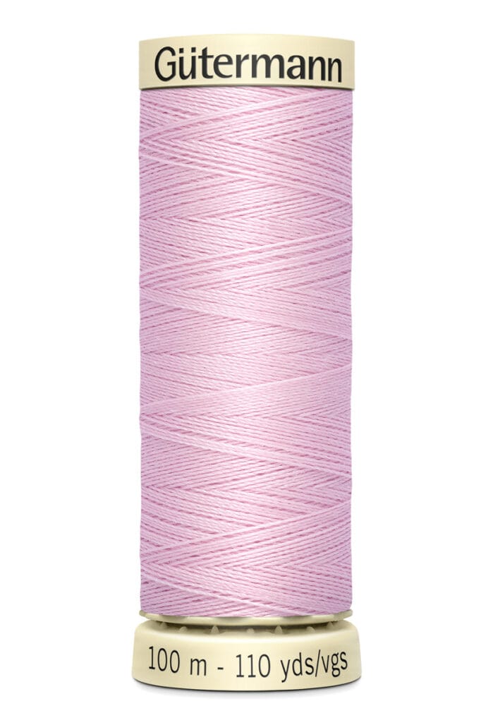 A spool of pale pink Gütermann sewing thread on a beige holder, labeled with "100 m - 110 yds/vgs".