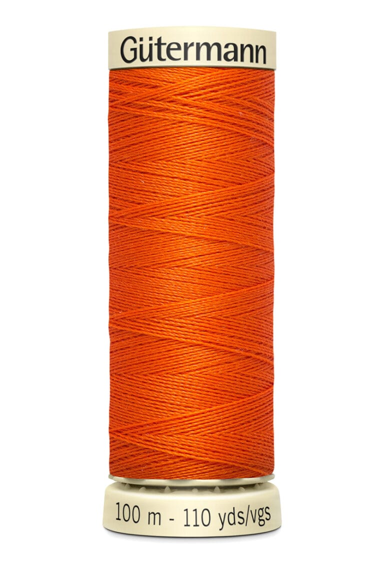 A spool of Gütermann orange sewing thread is shown, labeled with "100 m - 110 yds/vgs." The spool is off-white with the brand name printed at the top. The thread is tightly wound around the spool.