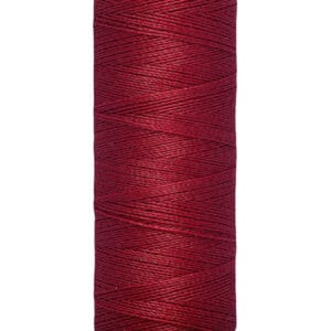 A spool of Gütermann red sewing thread with labels showing "100 m - 110 yds/vgs." The spool is beige at the top and bottom.