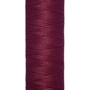 A spool of Gütermann sewing thread in a deep burgundy color. The label on top and bottom is cream-colored, featuring the brand name and measurement of 100 meters or 110 yards. The thread is neatly wound around the spool.