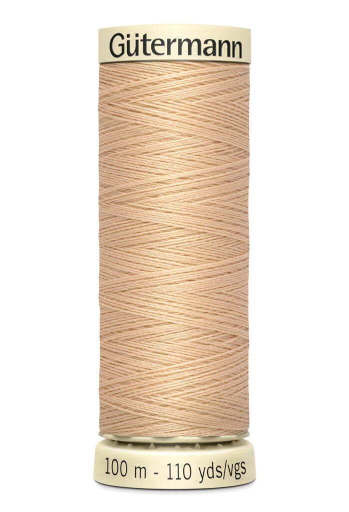 A spool of Gütermann beige sewing thread, labeled with "100 m - 110 yds," featuring tightly wound thread on a cylindrical holder.