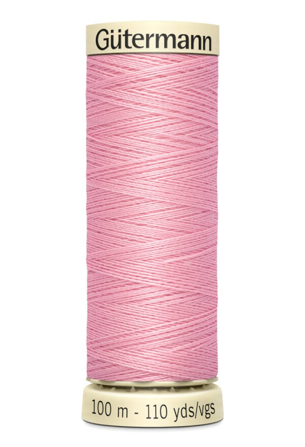 A spool of Gütermann pink sewing thread with white ends, labeled "Gütermann" on top. Text at the bottom reads "100 m - 110 yds." The thread is neatly wound, displaying a soft pink color.