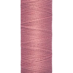 A spool of Gütermann thread in dusty rose color, with a label reading "100 m - 110 yds/vgs." The spool is cream-colored with the brand name printed at the top.