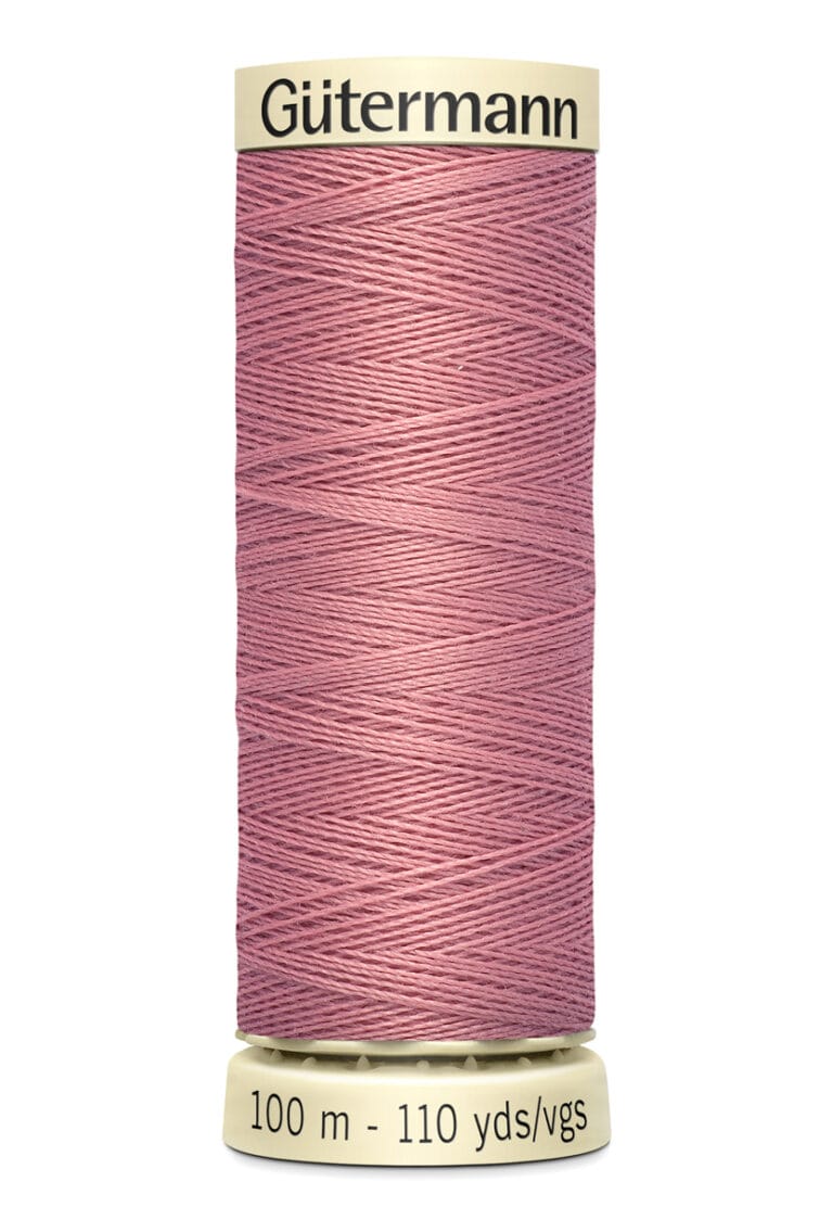 A spool of Gütermann thread in dusty rose color, with a label reading "100 m - 110 yds/vgs." The spool is cream-colored with the brand name printed at the top.