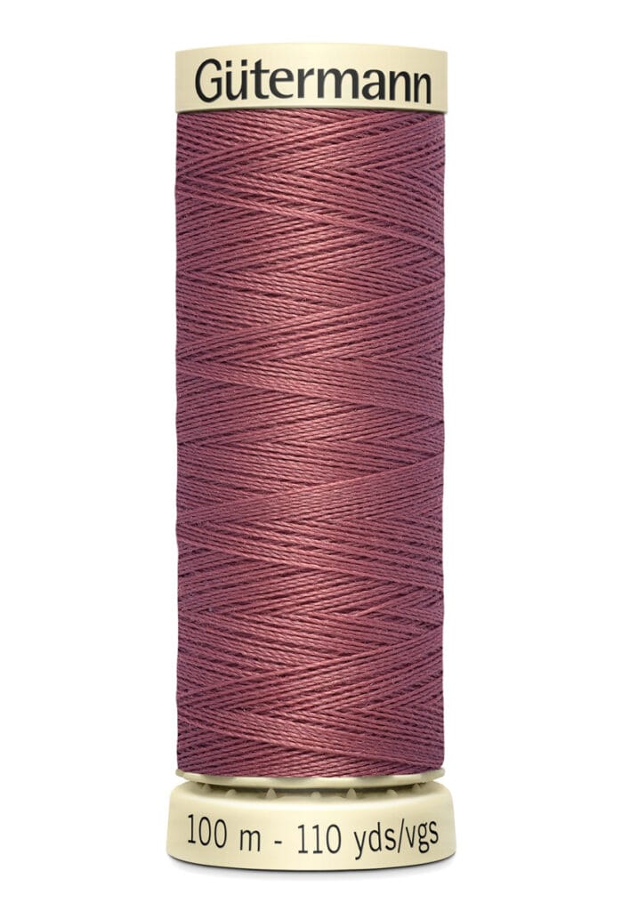 A spool of Gütermann thread in a muted mauve color. The spool holds 100 meters or 110 yards of thread. The base and top of the spool are cream-colored.