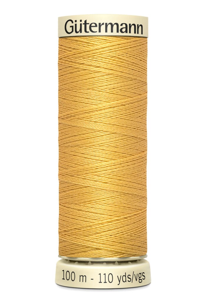 A spool of Gütermann sewing thread in a golden tan color, marked with "100 m - 110 yds/vgs," with black text on the label at the top and bottom. The thread is tightly wound around the spool.