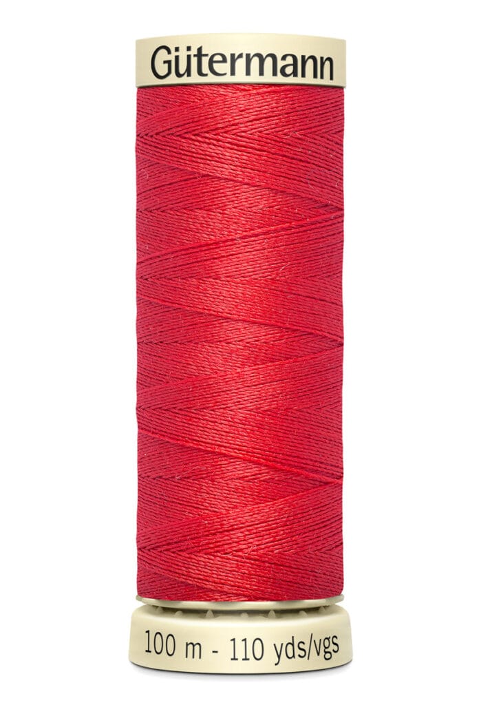 A spool of Gütermann red sewing thread, 100 meters or 110 yards, is displayed vertically. The thread is tightly wound around a beige spool with the brand name at the top.