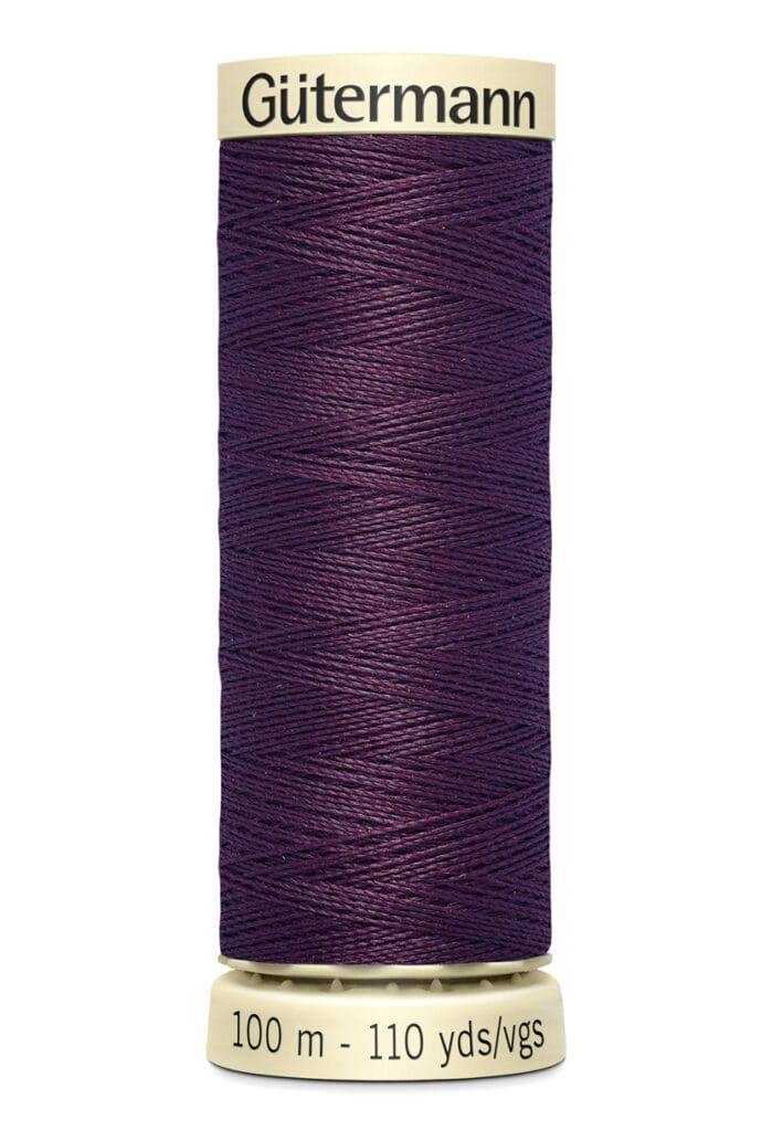 A spool of Gütermann sewing thread in dark purple, labeled to contain 100 meters or 110 yards of thread. The spool is cylindrical with a cream-colored top and bottom.