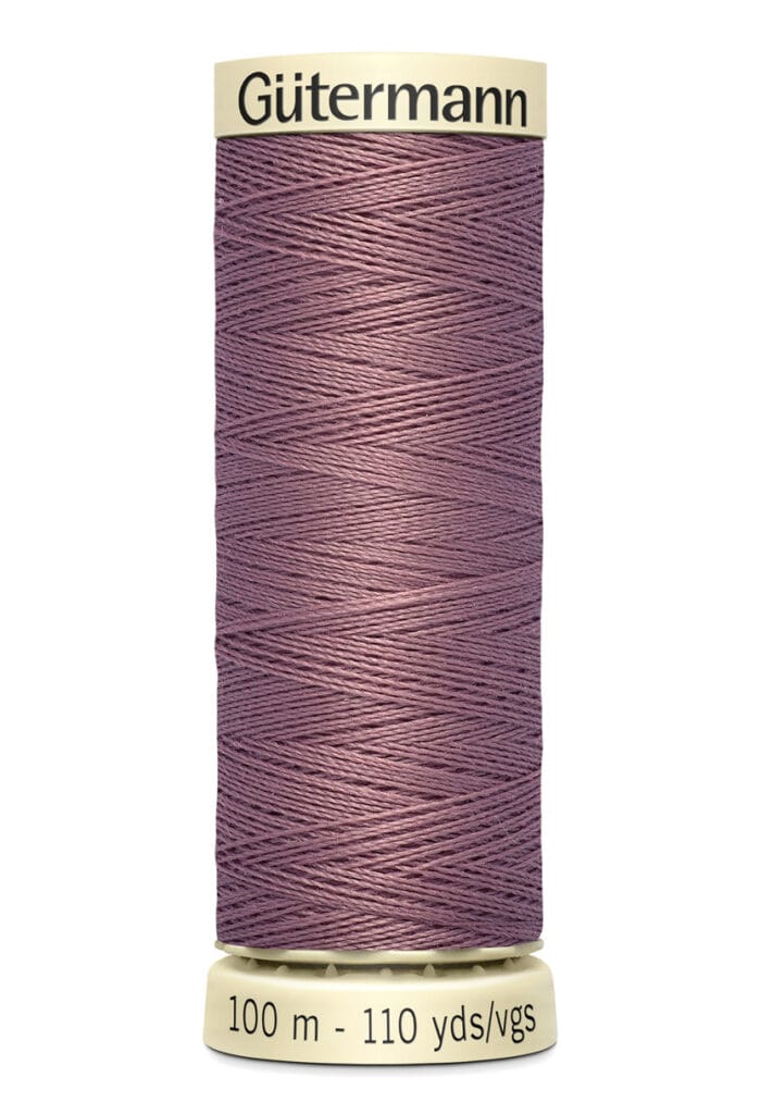 A spool of Gütermann sewing thread in a dusty purple color, wrapped neatly around a cream-colored cylindrical base. The label indicates the length as 100 meters or 110 yards.