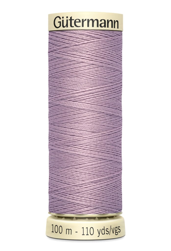 A spool of lilac-colored Gütermann sewing thread with a cream base and top. The label indicates a length of 100 meters or 110 yards.