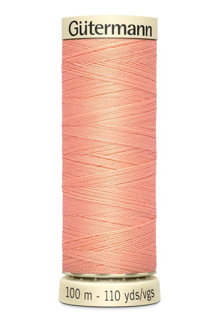 A spool of Gütermann sewing thread in a peach color. The label on the spool reads "100 m - 110 yds/vgs" indicating the length of the thread. The thread is wound neatly around the spool.