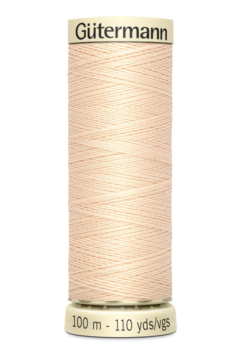 A spool of Gütermann thread with a soft beige color, labeled with 100 meters and 110 yards. The spool has a cream-colored top and bottom, displaying the brand name. The thread is neatly wound around the spool.