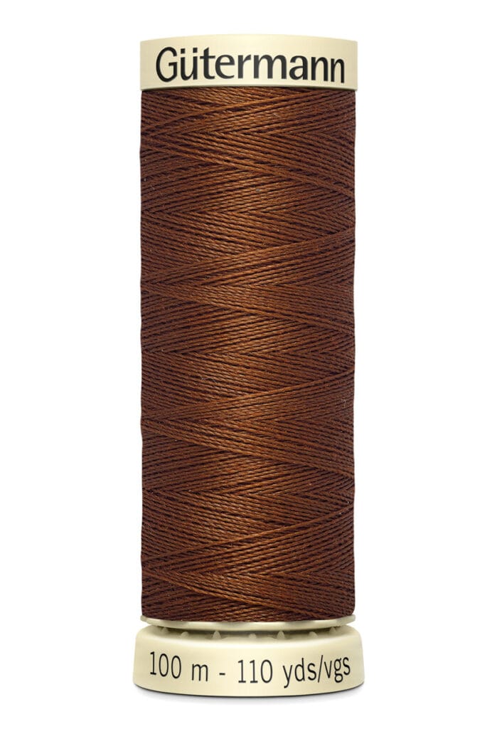 A spool of Gütermann thread, labeled as 100 meters or 110 yards. The thread is a rich brown color, neatly wound around the spool with beige ends.