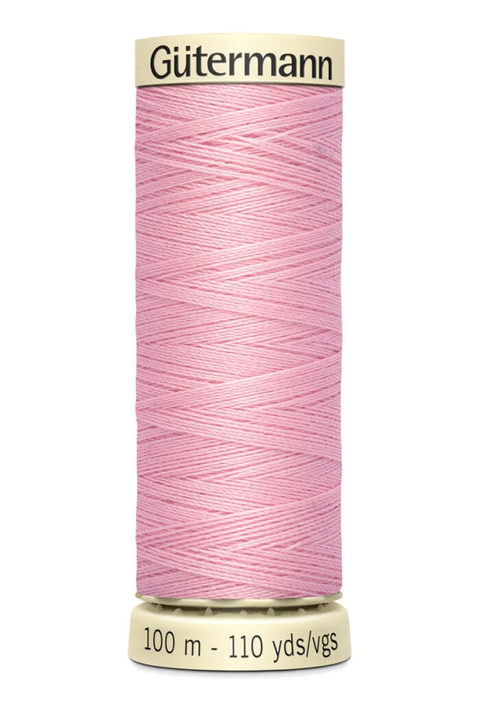 A spool of Gütermann thread in light pink, with a label showing 100 meters or 110 yards. The thread is neatly wound on a cream-colored spool.