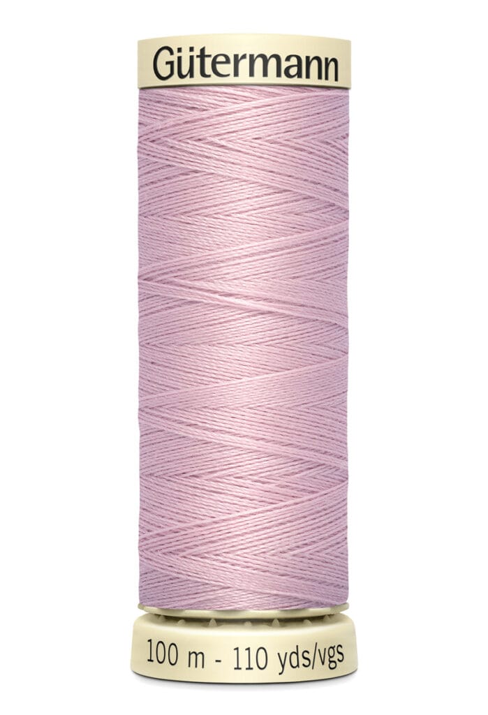 A spool of Gütermann sewing thread in light pink, showing 100 meters or 110 yards on the label, with a cream-colored top and base.