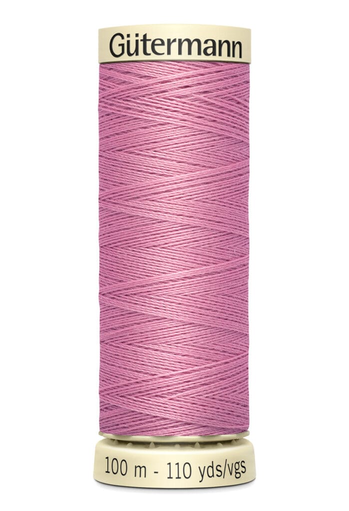 A spool of Gütermann thread in a pink color, with 100 meters (110 yards) of thread. The spool has a beige top and bottom with the brand name printed on the top and length details on the bottom.