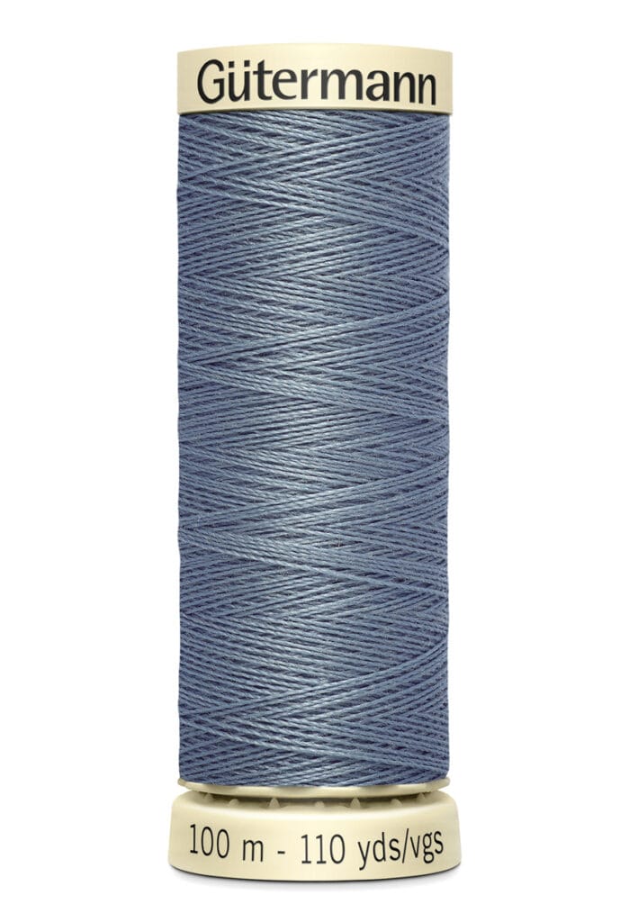 A spool of Gütermann sewing thread in denim blue. The spool is labeled with "100 m - 110 yds/vgs" and has a beige top and bottom. The thread is neatly wound and displayed against a plain white background.