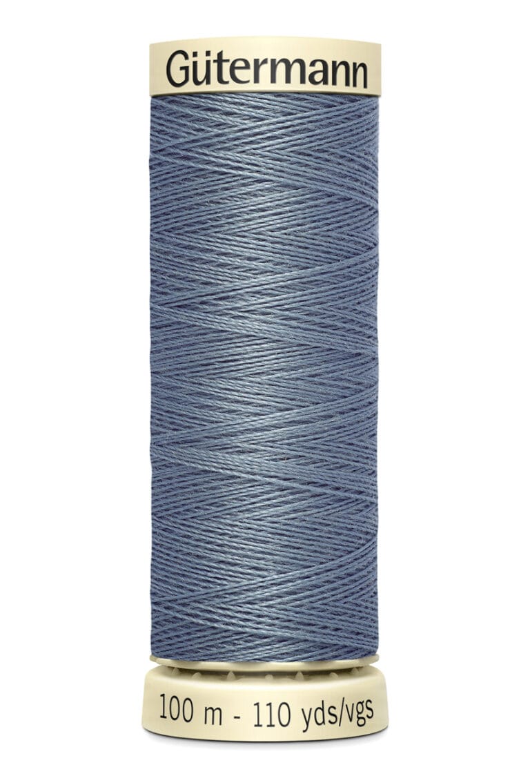 A spool of Gütermann sewing thread in denim blue. The spool is labeled with "100 m - 110 yds/vgs" and has a beige top and bottom. The thread is neatly wound and displayed against a plain white background.