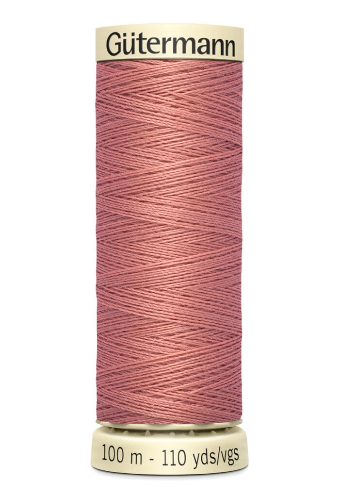 A spool of brownish-pink Gütermann sewing thread with cream-colored ends, labeled with "Gütermann" on the top and "100 m - 110 yds" on the bottom. The thread is neatly wound around the spool.