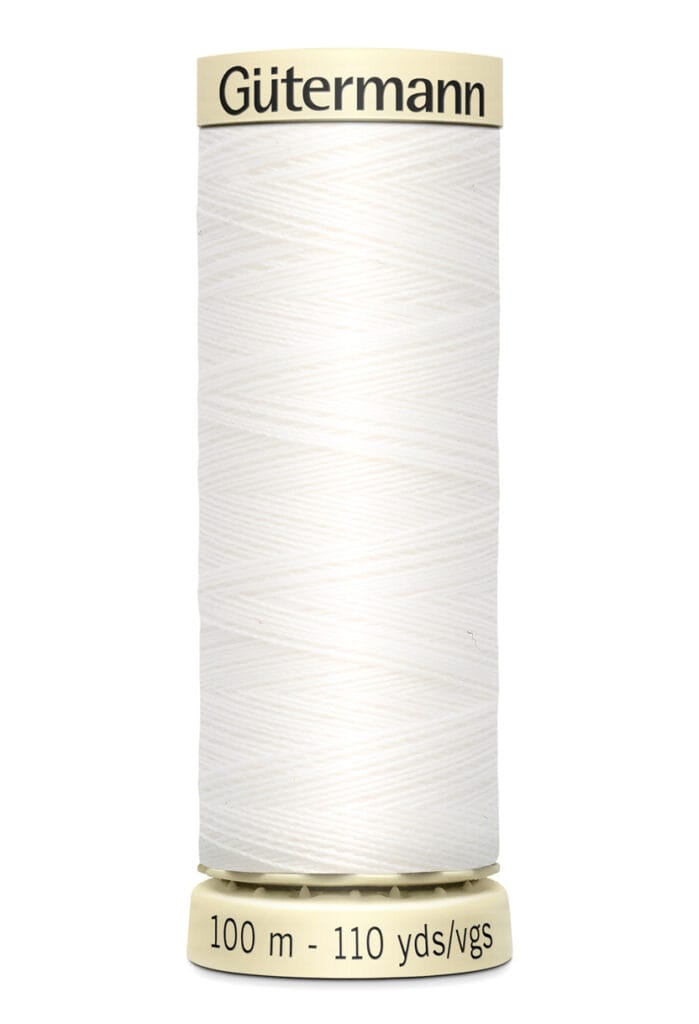 A spool of Gutermann thread with cream-colored thread wrapped around it. The label on top reads "Gütermann," and the base indicates "100 m - 110 yds/vgs.