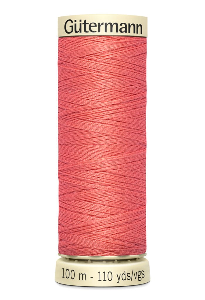 A spool of Gütermann thread in coral pink color, labeled with "100 m - 110 yds" on the base.