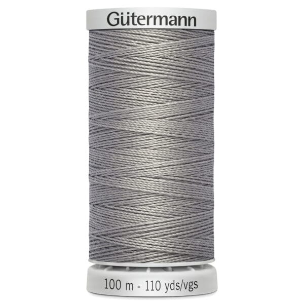 A spool of Gütermann thread in grey color, with a label indicating 100 meters or 110 yards. The spool is cylindrical, featuring a textured surface of tightly wound thread, and has white top and base caps with brand and measurement information.