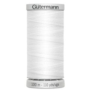 A spool of white Gütermann thread, labeled with "100 m - 110 yds/vgs," stands upright, showcasing its tightly wound texture.