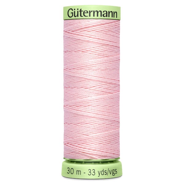 A spool of Gütermann sewing thread is shown, featuring light pink thread wrapped neatly around the spool. The label indicates 30 meters or 33 yards of thread. The spool is light green at the top and bottom.