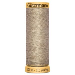 A spool of Gütermann sewing thread in light beige color. The spool is labeled with 100 meters and 110 yards. The top and bottom of the spool are golden yellow, and a zigzag pattern is visible on the thread.