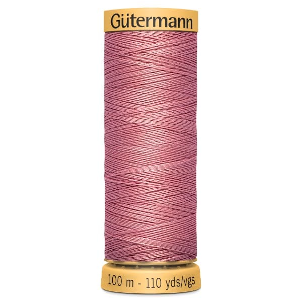 A spool of Gütermann thread with a pink color, designed for 100 meters or 110 yards. The thread is neatly wound on a cylindrical spool with yellow ends.