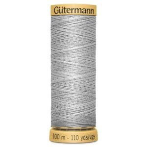 A spool of Gütermann sewing thread in light gray, labeled 100 meters or 110 yards. The spool has a yellow top and base, with the brand name on top. The thread is tightly wound in a crisscross pattern.