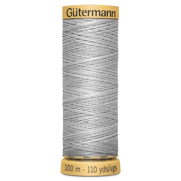 A spool of Gütermann sewing thread in light gray, labeled 100 meters or 110 yards. The spool has a yellow top and base, with the brand name on top. The thread is tightly wound in a crisscross pattern.