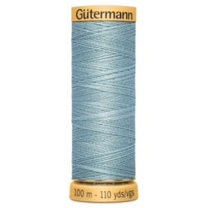 A spool of Gütermann thread in light blue color, labeled with "100 m - 110 yds/vgs." The spool has a yellow top and base with the brand name printed on it.