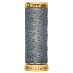 A spool of Gütermann sewing thread in a gray color. The spool has a yellow label with "Gütermann" written on top and indicates the thread length as 100 meters or 110 yards. The thread is tightly wound around the spool.