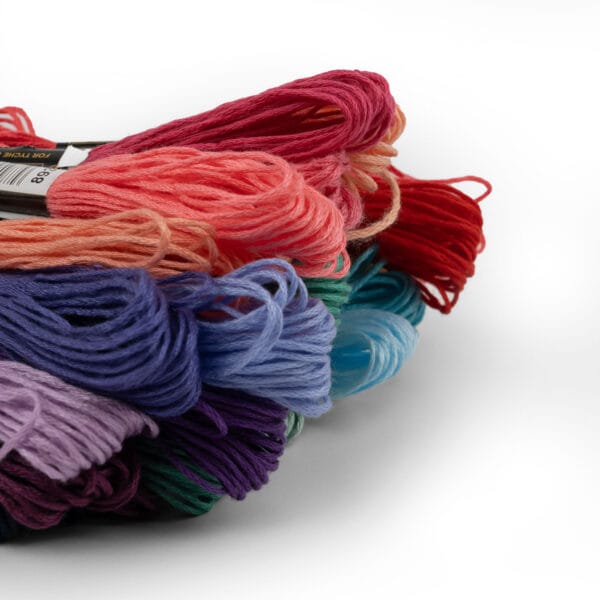 A close-up of various colored embroidery threads stacked together. The image showcases threads in shades of purple, blue, pink, red, and green, highlighting their texture and vibrancy against a white background.