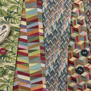 A collection of colorful ties featuring various patterns, including zigzags, geometric shapes, and leaves. Three buttons and part of a ceramic dish with a black and white illustration are visible on the left.