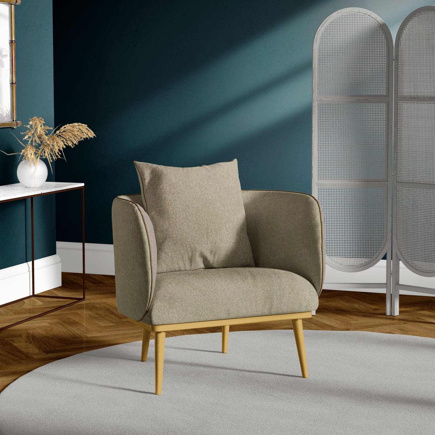 A cozy gray armchair with wooden legs sits on a light gray circular rug. The backdrop features a dark green wall, a white side table with dried plants, and a gray folding screen. The floor is a warm, brown wood.