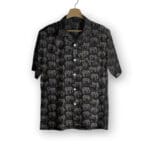 A black short-sleeve button-up shirt with a repeating pattern of outlined elephants in gray and white, hanging on a wooden hanger against a plain white background.