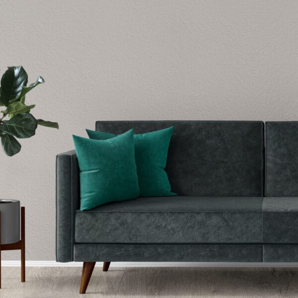 A modern dark green sofa with two teal throw pillows sits on a light wood floor, next to a small wooden side table with a potted plant, against a light gray wall.
